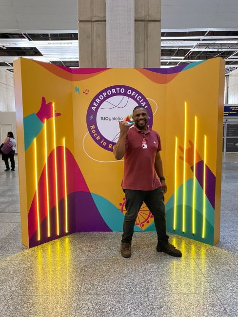 Painel de fotos do Rock in Rio com funcionário posando no Aeroporto Rio Galeão