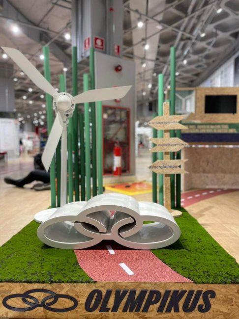 Cenografia Olympikus com pista de corrida vermelha, hélice e placas direcionais de madeira