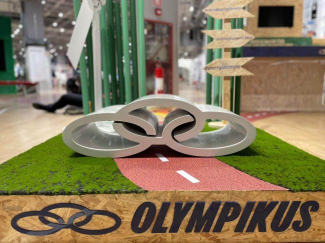 Cenografia Olympikus para ativação no ponto de venda: base com grama sintética, pista vermelha, logo Olympikus e peça em forma de nuvem