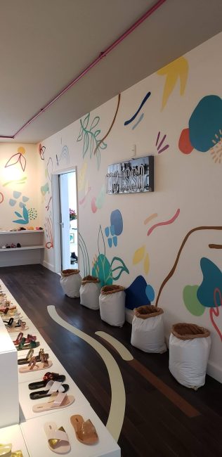 Loja pop-up Melissa Remake na Galeria 664: corredor com bancada de sapatos, vasos e parede ilustrada