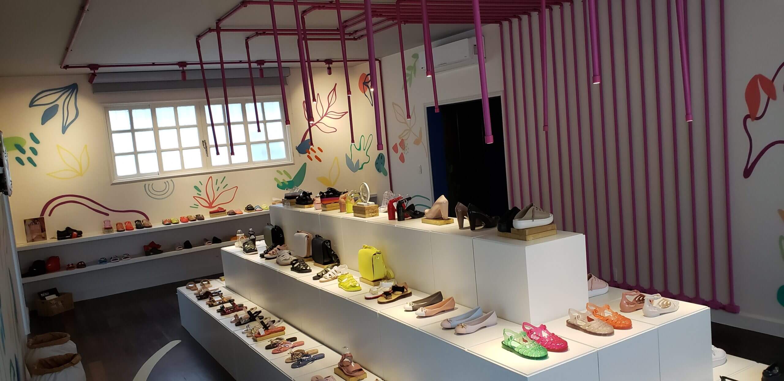 Loja pop-up Melissa Remake na Galeria 664: bancadas brancas com sapatos coloridos, tubulações rosa no teto e parede com grafismos