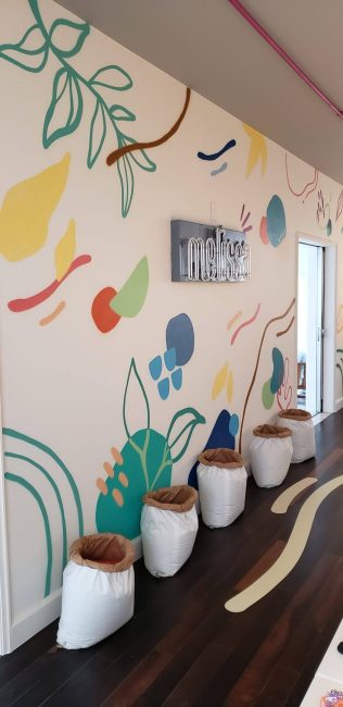 Parede com folhas e formas coloridas e vasos brancos na pop-up Melissa