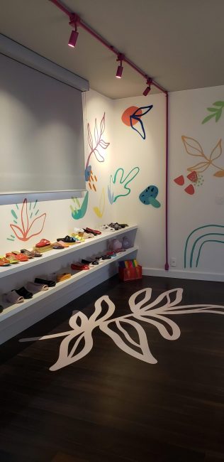 Piso escuro com desenho de folhas em branco e parede com grafismos na pop-up Melissa