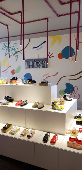 Loja pop-up Melissa Remake na Galeria 664: expositor em degraus com sapatos coloridos sob tubulação rosa