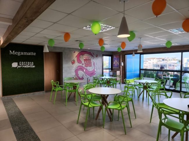 Área de mesas da Megamatte com cadeiras verdes e decoração de balões
