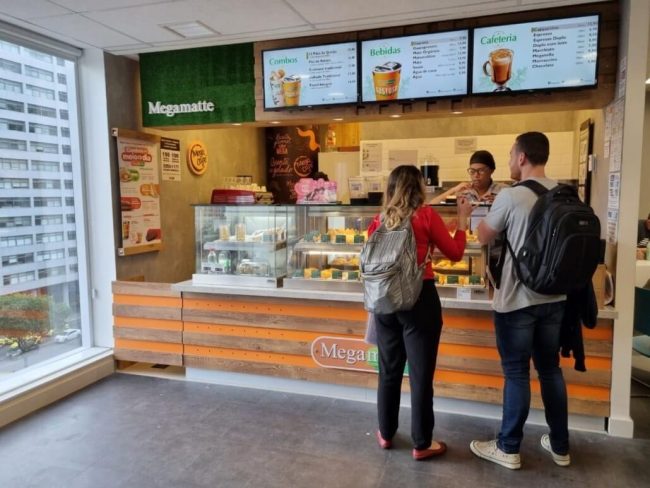 Clientes no balcão da Megamatte com cardápio digital em telas