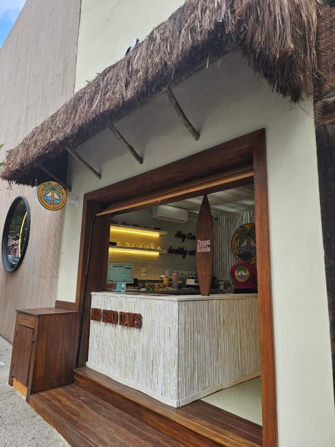 Fachada do bar Zaga Bowls em São Paulo, com cobertura de palha, balcão de madeira clara e acabamento rústico