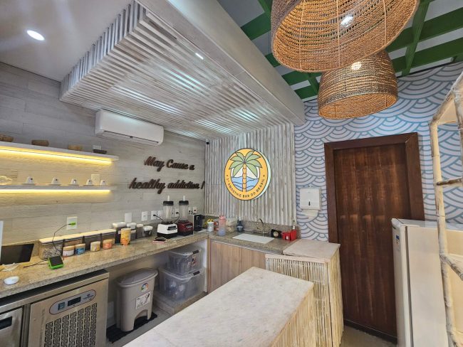 Cozinha e balcão de preparo do bar Zaga Bowls com forro ripado e letreiro na parede