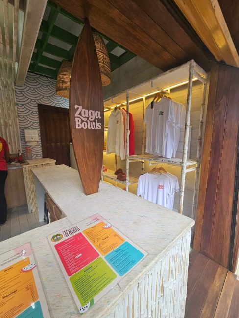 Balcão do Zaga Bowls com cardápios coloridos e araras de roupas ao fundo