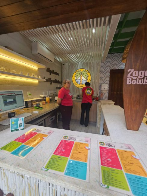 Balcão e cozinha do Zaga Bowls com cardápios coloridos sobre o balcão
