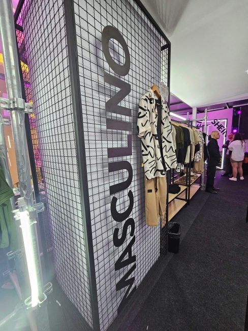 Parede de grade metálica com a palavra MASCULINO e peças expostas na pop-up Shein