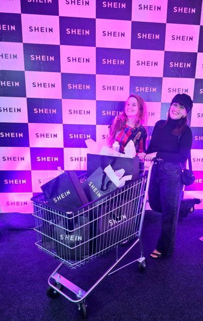Painel xadrez com logo Shein para fotos e cliente com carrinho de compras