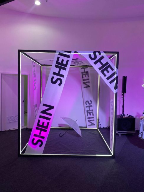 Cubo de estrutura metálica com fitas Shein iluminado em roxo