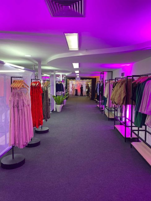 Corredor da pop-up Shein com araras de roupas e iluminação roxa