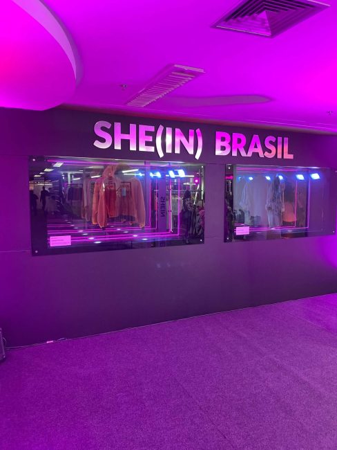 Parede preta com letreiro SHE(IN) BRASIL e vitrines na pop-up Shein