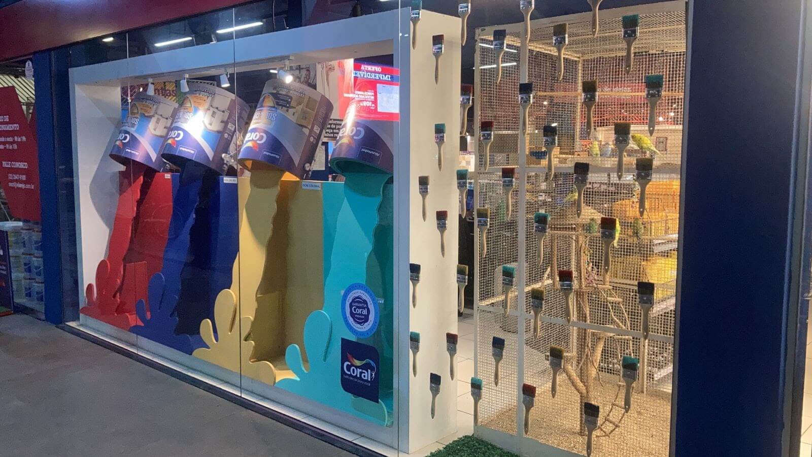 Vitrine Coral na loja Vilarejo em Cabo Frio, com latas de tinta derramando cores vermelha, azul, amarela e verde