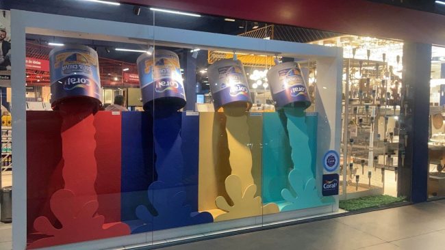 Vitrine Coral na loja Vilarejo em Cabo Frio: latas de tinta Coral escorrendo em vermelho, azul, amarelo e verde