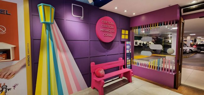Vitrine Coral Collab Barbie vista pelo corredor do shopping, com banco e poste de luz