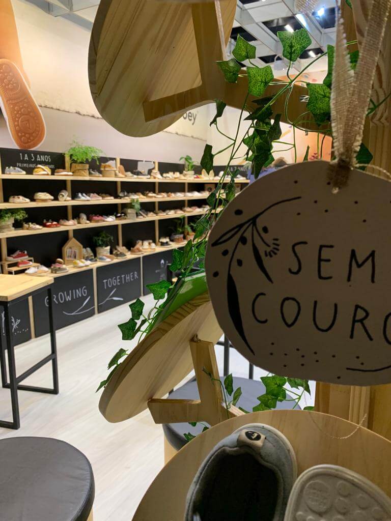 Stand Tip Toey Joey na Feira Ópera: prateleiras de madeira com sapatos infantis e etiqueta "sem couro"