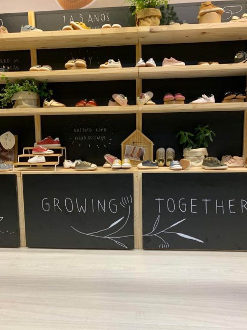 Stand Tip Toey Joey na Feira Ópera: prateleiras cheias de sapatos infantis com plantas decorativas e "growing together"